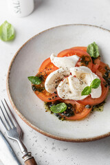 Caprese salad in modern feed with tomatoes, basil, mozzarella, pesto close up. Traditional Italian food with cutlery on white background, menu