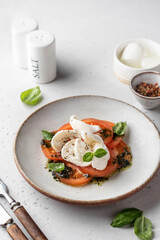 Caprese salad in modern feed with tomatoes, basil, mozzarella, pesto. Traditional Italian food with cutlery on white background, menu