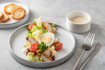 Caesar salad in modern linear feed with chicken, egg, tomatoes, lettuce and parmesan chips with cutlery on gray table, menu
