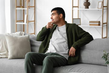 Fototapeta premium Thoughtful young man sitting on sofa at home