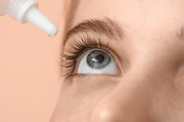 Young woman using eye drops on beige background, closeup