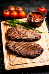 Grilled steak on a cutting board with rosemary and tomatoes. 