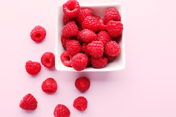 Bowl of fresh ripe raspberry on pink background, closeup