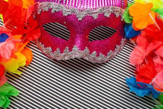 pink carnival mask on a black and white striped background and colorful  flowers