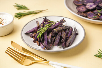 Plate with sticks of fried purple potatoes on color background