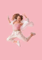 Young woman in earphones with mobile phone dancing on pink background