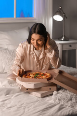 Young woman with boxes of tasty pizza in bedroom at night