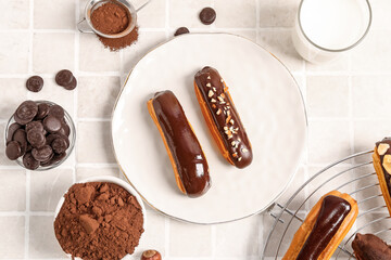 Composition with plate of tasty eclairs, chocolate drops and cocoa powder on light tile