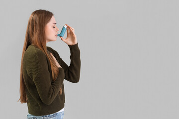 Young woman with inhaler on  grey background