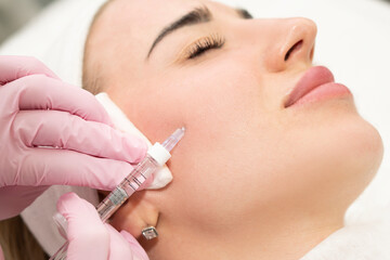 Close-up of the hands of an experienced cosmetologist injecting beauty into a woman's face. Filler...