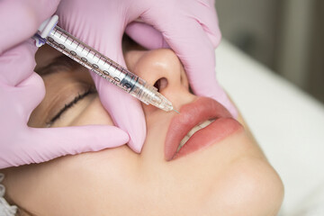 Obraz na płótnie Canvas Lip augmentation and correction procedure in a cosmetology salon. The specialist makes an injection in the patient lips.