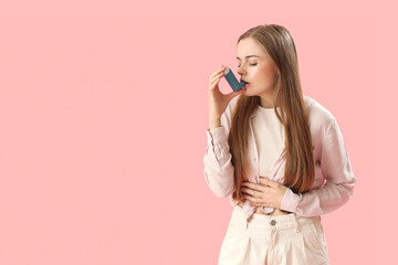 Sick young woman with inhaler on pink background