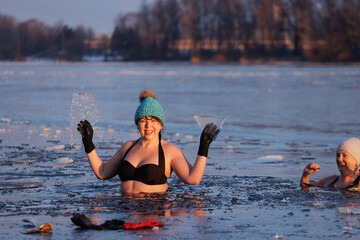 Two women stand at the river's edge as the sun rises, having just finished a winter swim. The cold...