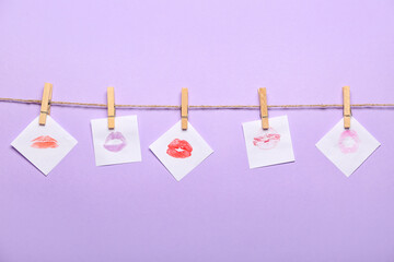 Rope, clothespins and paper sheets with lipstick kiss marks on lilac background