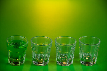 Shot glasses lined up against emerald theme background filled with green spirit cocktail to be...