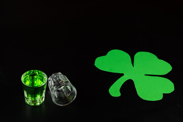 Shot glasses and shamrock with black background filled with emerald green spirit cocktail to be...