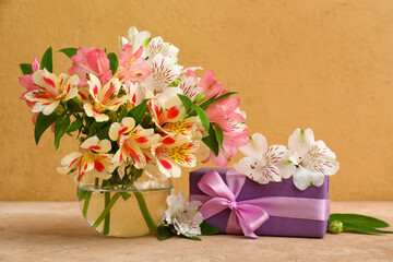 Vase with beautiful alstroemeria flowers and gift box on color background. Mother's day celebration