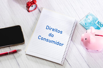 A palavra Direitos do Consumidor escrita em um caderno que está sobre uma mesa de madeira. Um nota...