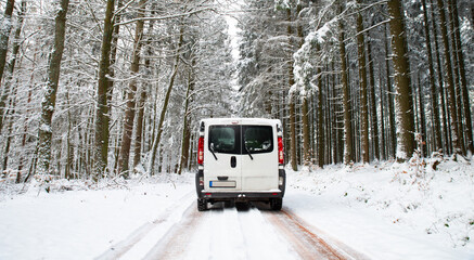 Camper Van  driving  on a road through a snow covered forest in winter, adventure vacation and lifestyle in the woodlands, Germany