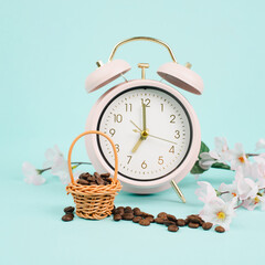 Wicker basket with roasted coffee beans, an alarm clock and cherry blossom, wake up in the morning, spring season

