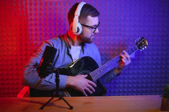 Close up man in headphones playing guitar and singing, recording on smartphone, musician artist recording new song video for social network, blogger or music teacher shooting course in home studio