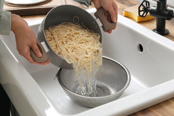 Woman pouring water from boiled spaghetti into colander in sink, closeup