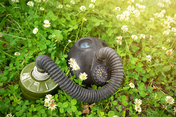 A rubber gas mask with a trunk lies in the green grass with white flowers. Harmful emissions into...