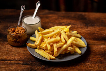 French fries on a plate on a wooden background. Mayonnaise and sauce stand side by side. Vegetarian food.