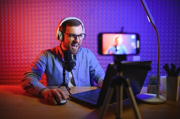 A video blogger records content in his studio. The host of the video blog is a young man who is...