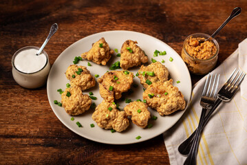 Cauliflower wings food. Pieces of cauliflower cooked in batter on a plate on a wooden background. Sprinkled with green onions.