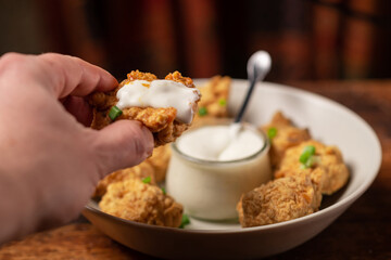 Cauliflower wings food. Pieces of flour-fried cauliflower with vegan sauces on a plate. A man's hand is holding a piece.