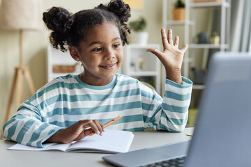 Cute black girl with pigtails waving to camera in online class