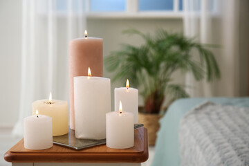 Fototapeta na wymiar Burning candles on end table in bedroom, closeup