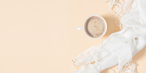 Spring trendy composition. White soft scarf and  cup of coffee on light beige isolated background. Flat lay, top view, copy space