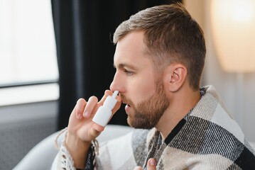 Sick man with nasal spray and paper tissue at home - obrazy, fototapety, plakaty