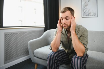 Ill man sitting on his bed with his head on his hand