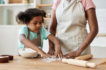 Cute black girl baking with mom in kitchen and playing with flour