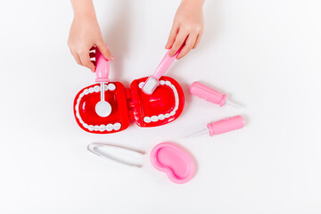 Kids hands with dentist set toy. White background. Flat lay. Medical, stomatology, kids toys concept. Profession choice.