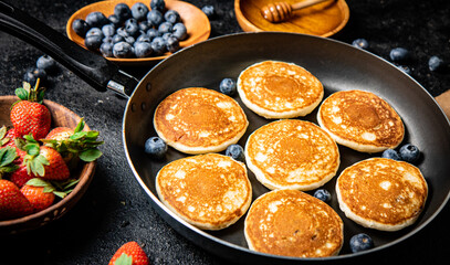 Pancakes in a frying pan with fresh berries and honey. 