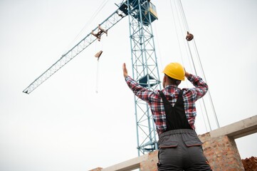 Communicating with crane guy. Construction worker in uniform and safety equipment have job on building.