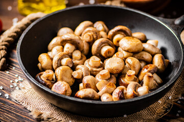 Frying pan with fried mushrooms on a wooden tray. 