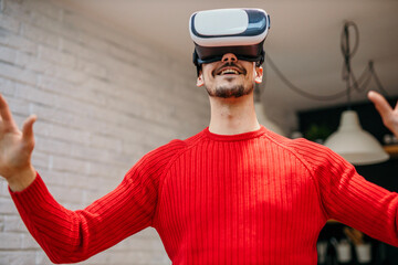 Low angle view of a surprised handsome young man wearing a virtual reality headset, playing a virtual reality game at home.