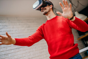Low angle view of a handsome young man wearing a virtual reality headset, playing a virtual reality...
