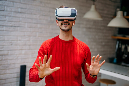 Handsome man wearing a VR headset resting at home in the living room alone using futuristic technology making gestures with hands in the air, and playing 3D video games. Virtual reality glasses