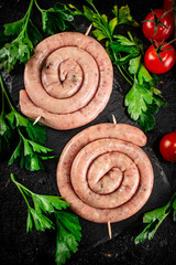 Fototapeta na wymiar Raw sausages on a stone board with parsley and tomatoes. 