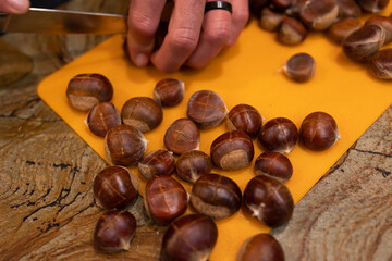 A horizontal photo a caucasian young man preparing  brown Chestnuts for roasting by cutting X's in the roasted nuts with a long knife. 