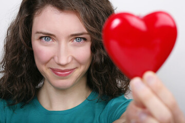 Portrait of attractive happy young woman holding up plastic heart against white background.