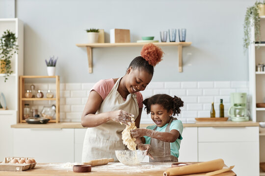 Happy black mother and daughter playing with dough baking together