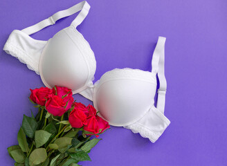 Top view white lace lingerie with red roses on violet background. Set of woman essential underwear...
