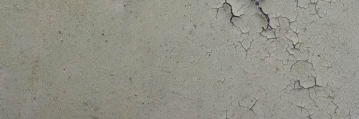 Peeling paint on the wall. Panorama of a concrete wall with old cracked flaking paint. Weathered rough painted surface with patterns of cracks and peeling. Panoramic texture for background and design.
